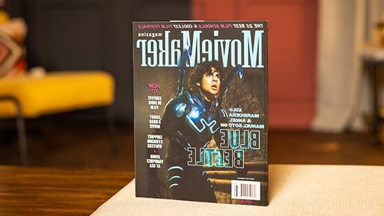 桌上放着一本《十大菠菜台子》杂志. 封面上是一个穿着蓝色甲壳虫服装的演员. 标题是“25所最佳电影学院” & “最酷的电影节”横贯顶部.
